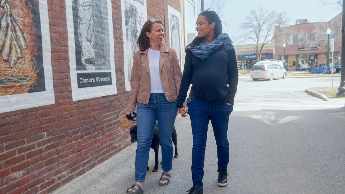 Two women, holding hands, strolling by murals. 