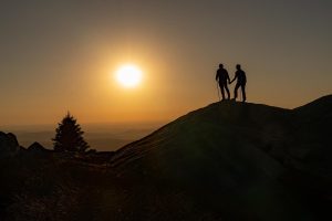 Couple holds hands on a mountain top at sunset
