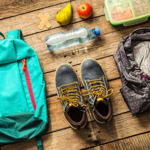 Gear laid out for hiking: shoes, first aid, water, snacks, backpack