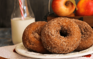 Cider donuts on a plate with a glass of milk and fruit in the background